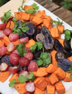 white platter filled with colorful root vegetables and side bowl of creamy sauce